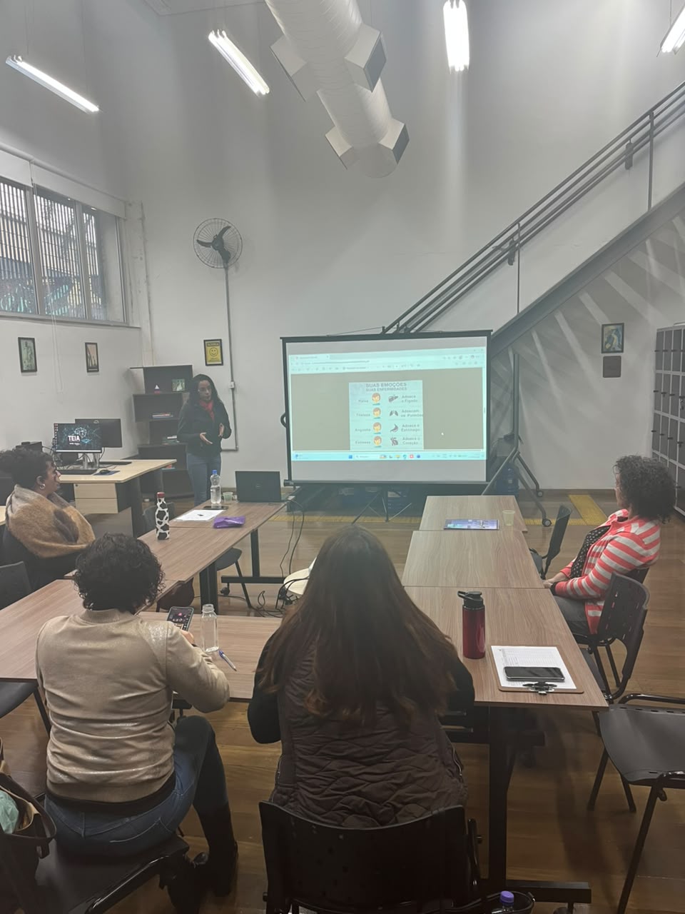 Turma acompanhando a palestra, slide 'Suas emoções, suas enfermidades'